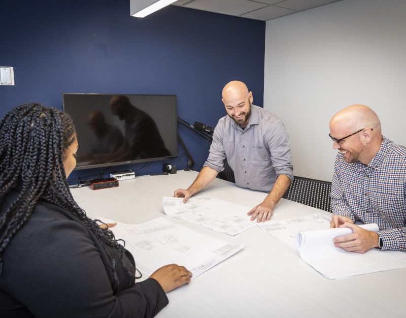 Motz Engineering colleagues smiling as they review architectural blueprints around a conference table